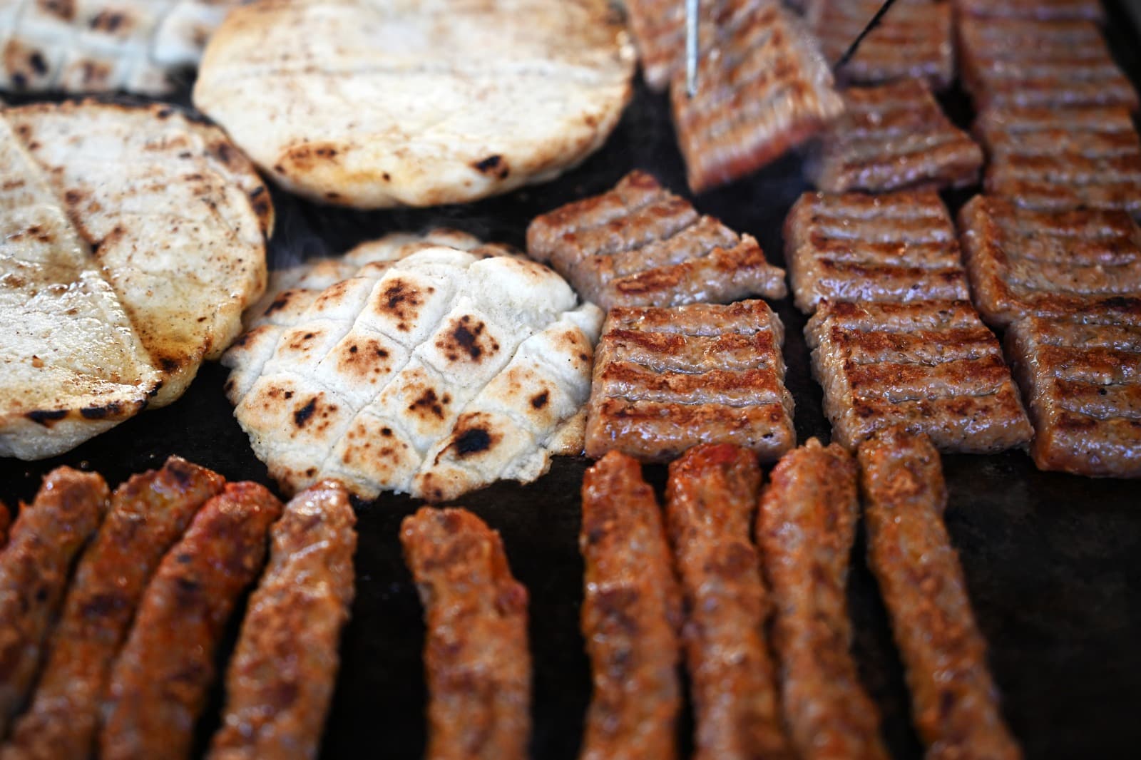 Ćevapi on the grill — fire, char, lepinja.