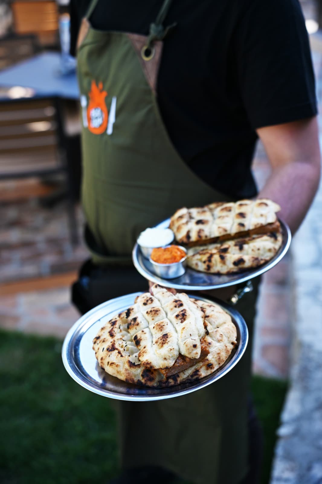 Server carrying two plates of ćevapi with lepinja, kajmak and ajvar.